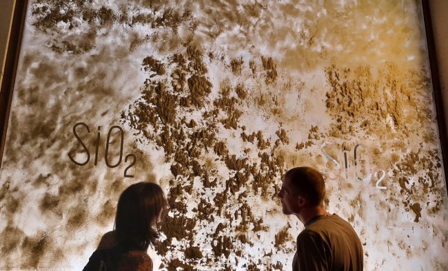 Two people are looking at a window covered in sand.
