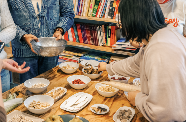 table with some ingredients for cantonese soup. some people around the table picking ingredients and putting them in their own bowls